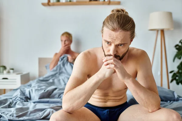 Decepcionado gay hombre en calzoncillos sentado cerca novio en borrosa fondo en dormitorio - foto de stock