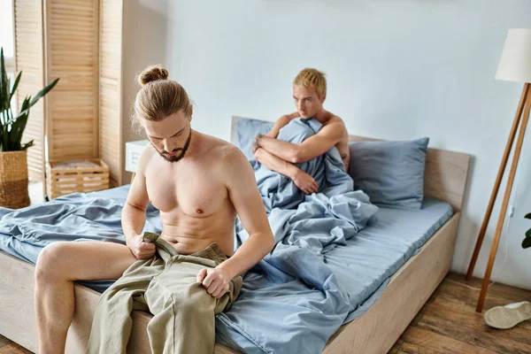Bärtiger schwuler Mann verkleidet sich in der Nähe beleidigter Liebespartner morgens im Schlafzimmer, Problembeziehung — Stockfoto