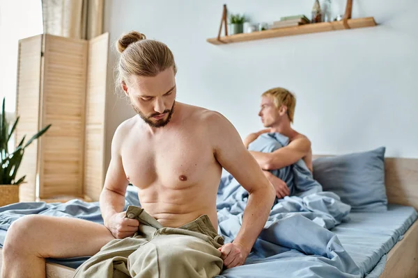 Bearded gay man dressing up near offended love partner in bedroom in morning, trouble relationship — Stock Photo