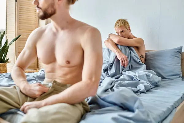 Beleidigter schwuler Mann sitzt und den Liebespartner ansieht, der sich im Schlafzimmer verkleidet, Beziehungsprobleme — Stockfoto