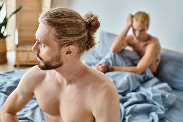 Розчарований бородатий гей чоловік, дивлячись далеко від розмитої спальні хлопця, труднощі у відносинах — стокове фото