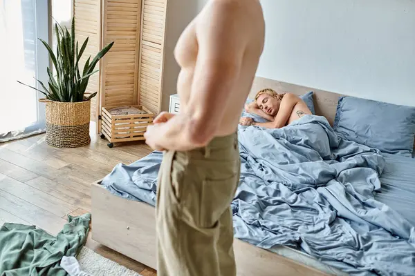Gay man standing and dressing up near love partner sleeping in bedroom in morning, love conflict — Stock Photo