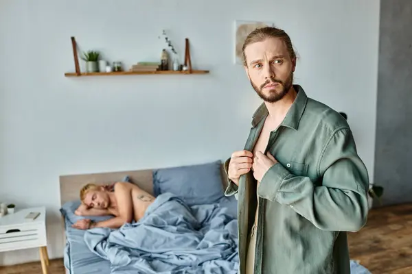 Frustrierter bärtiger schwuler Mann verkleidet sich in der Nähe von Freund, der morgens im Schlafzimmer schläft, Liebeskonflikt — Stockfoto