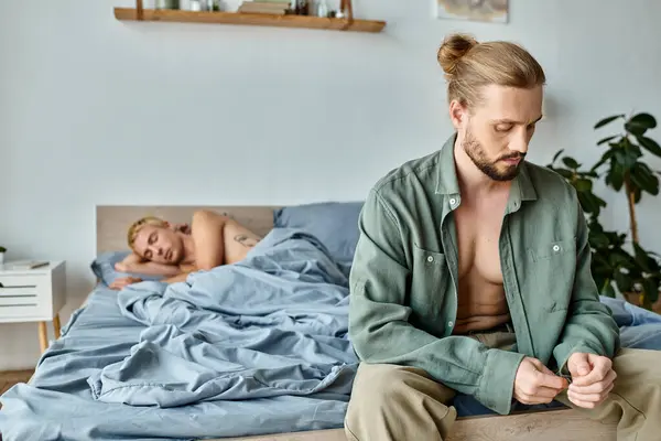 Offeso barbuto gay uomo seduta e vestirsi vicino fidanzato sdraiato in camera da letto in mattina — Foto stock