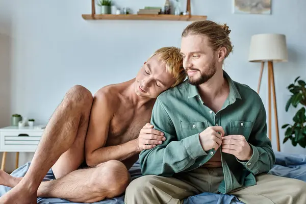 Happy gay man leaning on smiling bearded boyfriend sitting in modern bedroom, happiness — Stock Photo