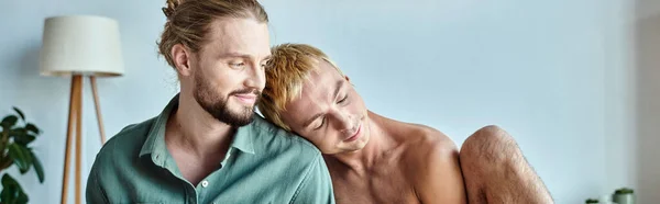 Glücklicher schwuler Mann, der sich auf lächelnden bärtigen Freund stützt, der im modernen Schlafzimmer sitzt, Banner — Stockfoto