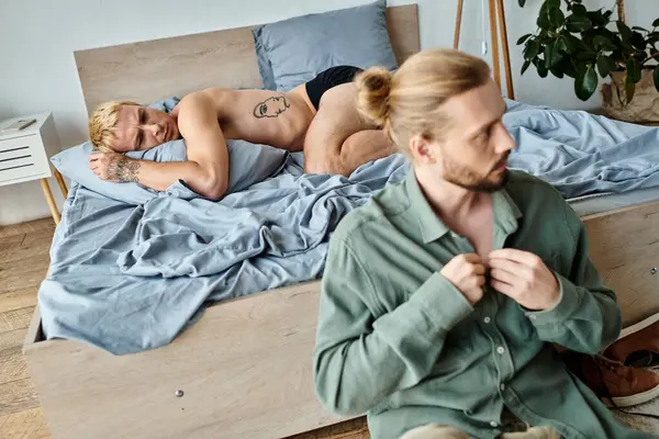 Aufgebracht bärtiger schwuler Mann verkleidet sich in der Nähe eines enttäuschten Freundes, der im Schlafzimmer liegt, Liebesprobleme — Stockfoto