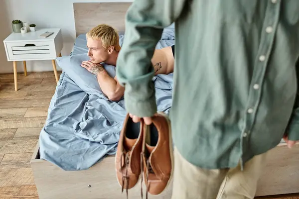 Offended tattooed gay man lying on bed while his partner leaving bedroom in morning, love conflict — Stock Photo