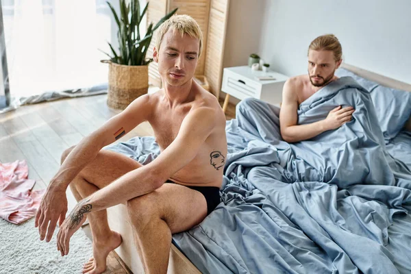 Beleidigter tätowierter Schwuler sitzt morgens neben Freund im Bett, Beziehungsschwierigkeiten — Stockfoto