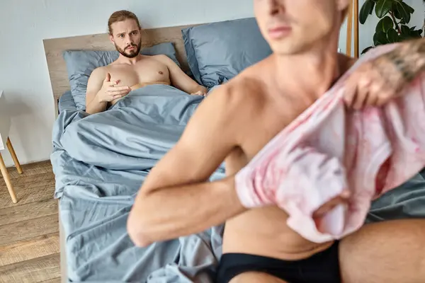 Desenfocado gay hombre vestirse hasta cerca decepcionado novio acostado en dormitorio, problemático relación - foto de stock