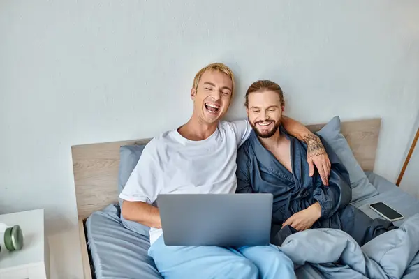 Gai gay couple regarder film sur portable et rire sur lit, heureux amour et relations — Photo de stock