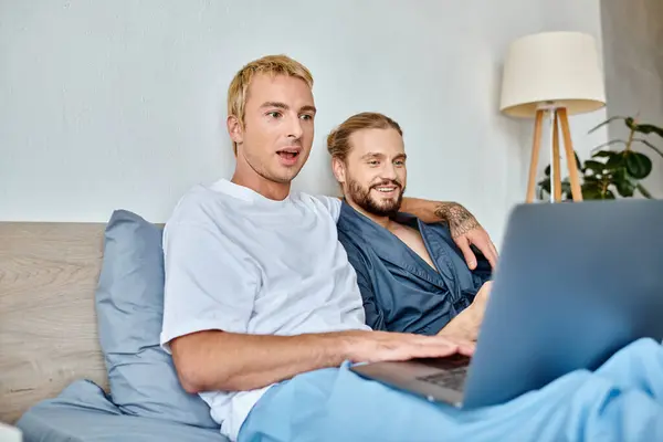 Erstaunt gay Mann beobachten Film auf Laptop in der Nähe lächelnden bärtigen Freund auf Bett Freizeit im Schlafzimmer — Stockfoto