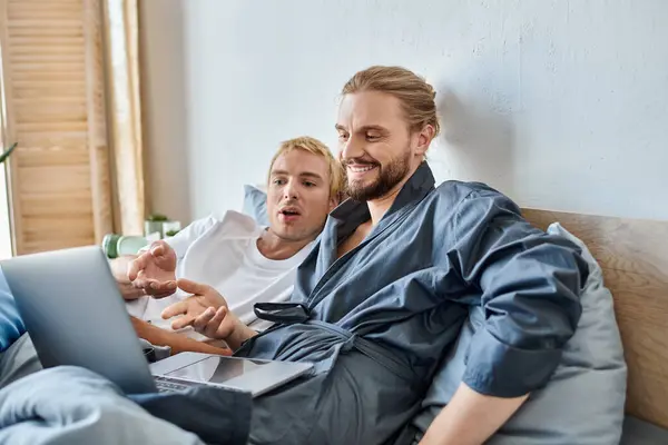 Stupito e allegro gay coppia indicando a laptop mentre guardando film in camera da letto, felice svago — Foto stock