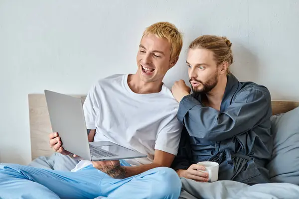 Laugh gay man showing laptop to amazed bearded man sitting with coffee cup in bedroom, leisure — Stock Photo
