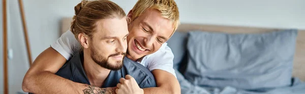 Freudig tätowierter schwuler Mann umarmt bärtigen Freund lächelnd im Morgenschlafzimmer, horizontales Banner — Stockfoto