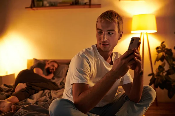 Unfaithful gay man chatting on mobile phone near love partner sleeping at night in bedroom — Stock Photo
