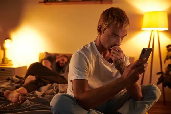 Unfaithful gay man chatting on mobile phone near love partner sleeping at night in bedroom — Stock Photo