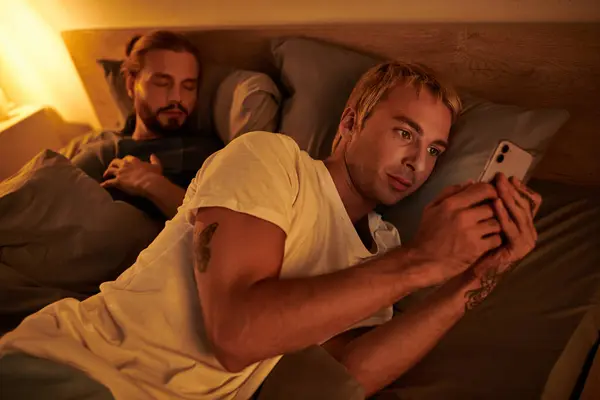 Homme gay déloyal messagerie sur téléphone mobile près de petit ami dormir la nuit dans la chambre, tricherie — Photo de stock