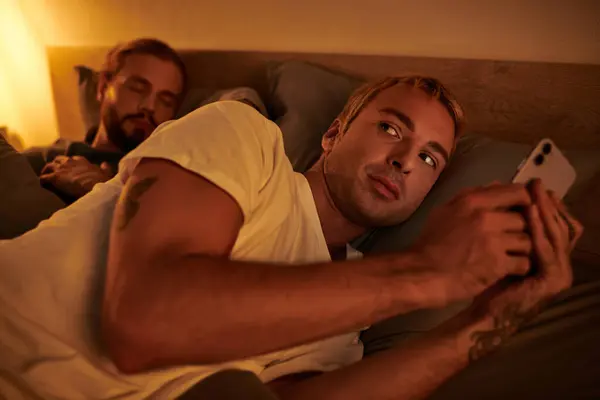 Gay homme infidèle messagerie sur téléphone mobile près petit ami dormir la nuit dans chambre, tricherie — Photo de stock