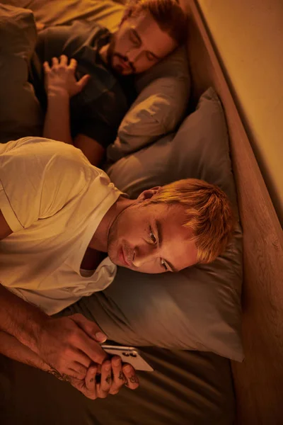 Unfaithful gay man messaging on mobile phone near boyfriend sleeping at night in bedroom, cheating — Stock Photo