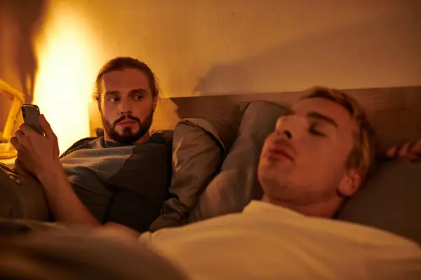 Unfaithful bearded gay messaging on mobile phone near sleeping boyfriend at night in bedroom — Stock Photo