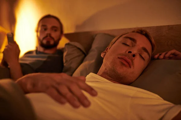 Gay man sleeping near unfaithful boyfriend browsing date app on smartphone at night in bedroom — Stock Photo