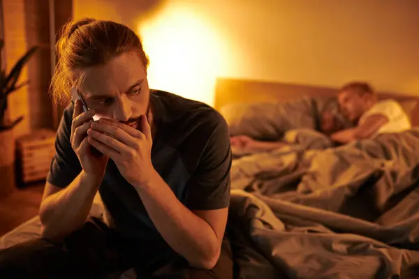Desleal gay hombre hablando en móvil mientras su amor pareja durmiendo en la noche en dormitorio - foto de stock