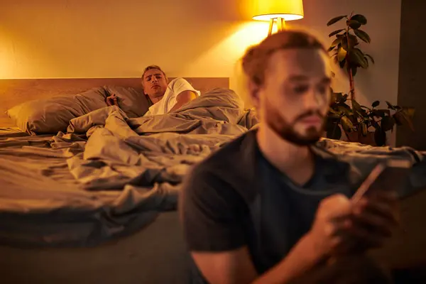 Découragé gay homme regarder copain messagerie sur téléphone mobile dans chambre à coucher la nuit, tricherie — Photo de stock