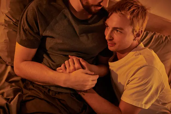 Tattooed gay man smiling with closed eyes near happy bearded boyfriend at night in bedroom, gay date — Stock Photo