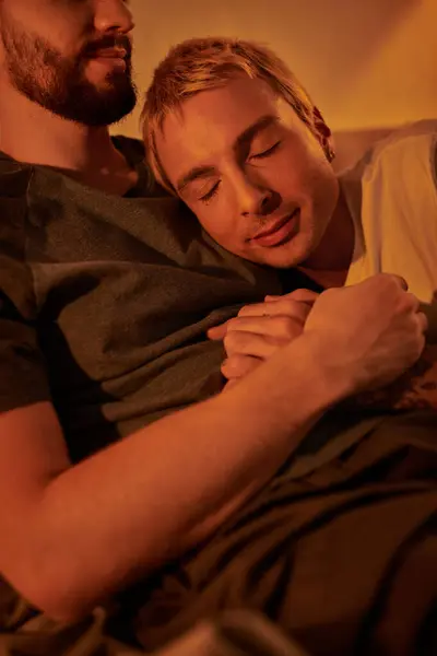 Hombre gay tatuado durmiendo en el pecho de novio barbudo en la noche en el dormitorio, amor y serenidad - foto de stock