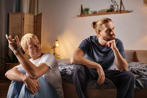 Gay l'homme parler à bouleversé et offensé amour partenaire assis la nuit dans chambre à coucher troublé amour — Photo de stock