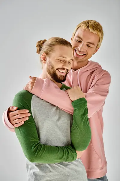 Fröhliches schwules Paar in stilvoller Freizeitkleidung, das sich vor grauem Hintergrund umarmt, harmonische Beziehung — Stockfoto