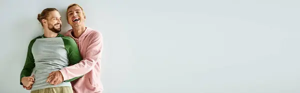 Excited gay man holding hands of bearded boyfriend and laughing on grey backdrop, horizontal banner — Stock Photo