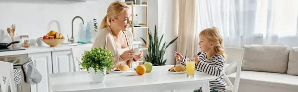 Fille mignonne petit déjeuner avec mère blonde heureuse dans la cuisine moderne, bannière de style de vie — Photo de stock