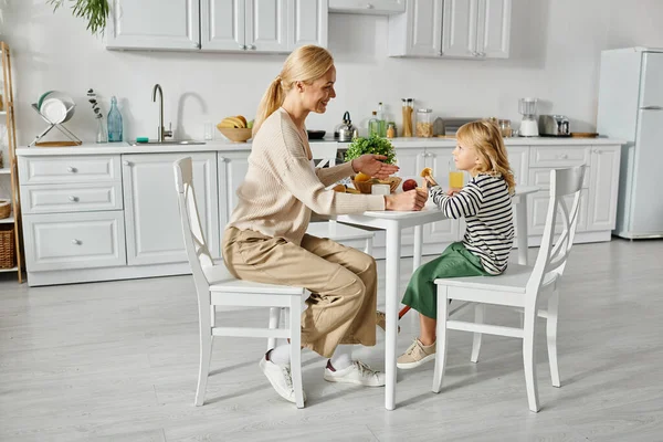 Mãe feliz tomando café da manhã com sua filhinha com perna protética na cozinha, inclusão — Fotografia de Stock