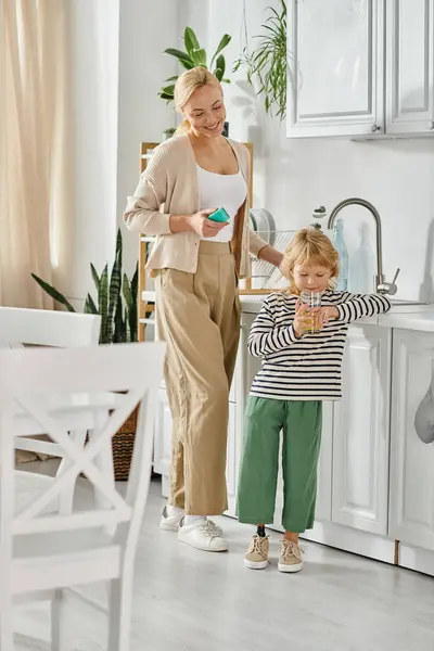 Menina bonito com prótese perna beber suco de laranja perto feliz mãe lavar pratos na cozinha — Fotografia de Stock
