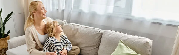 Радісна мати обіймає дочку в повсякденному вбранні і сидить разом на дивані у вітальні, банер — стокове фото