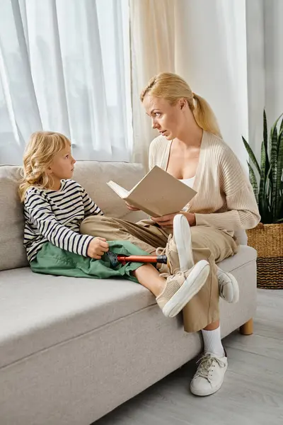 Attractive mother reading book to daughter with prosthetic leg while sitting together in living room — Stock Photo