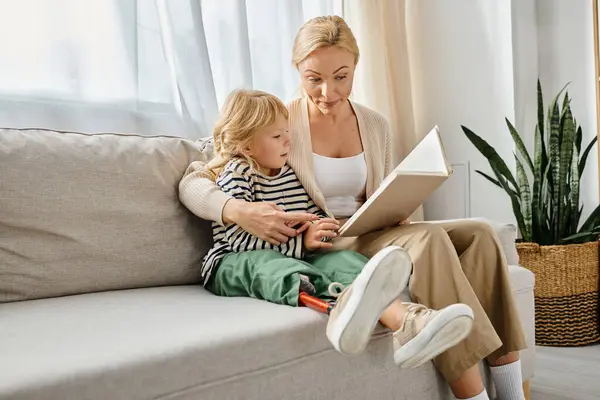 Blonde woman reading book to daughter with prosthetic leg while sitting together in living room — Stock Photo