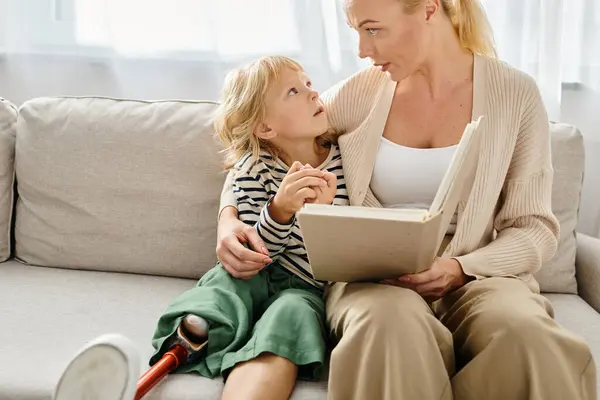 Blonde mother reading book to her kid with prosthetic leg while sitting together in living room — Stock Photo