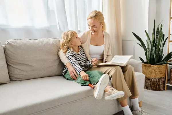 Mãe feliz ler livro para sua filha com perna protética e sentados juntos na sala de estar — Fotografia de Stock