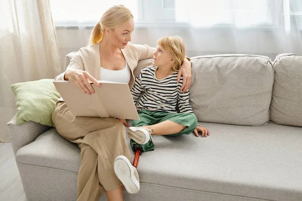 Mutter liest ihrem aufmerksamen Kind mit Beinprothese Buch und sitzt zusammen im Wohnzimmer — Stockfoto