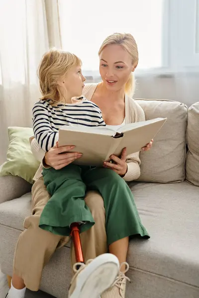 Joyeuse fille avec prothèse jambe assise sur les tours de mère blonde et livre de lecture dans le salon — Photo de stock