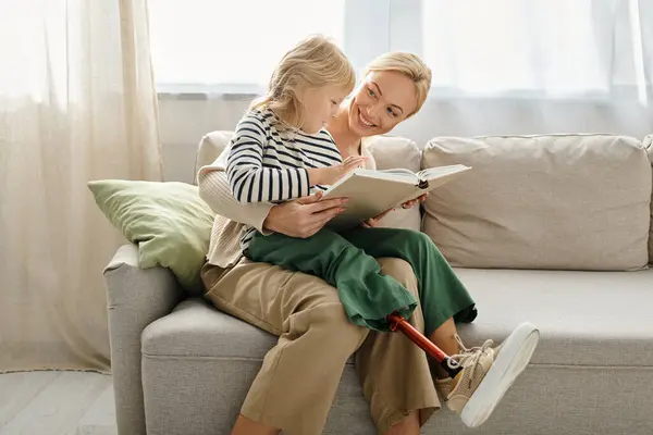 Fröhliches Mädchen mit Beinprothese sitzt auf dem Schoß einer blonden Mutter und liest Buch im Wohnzimmer — Stockfoto