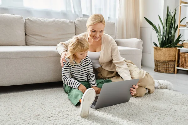 Happy child with prosthetic leg using laptop and sitting on carpet with mother in living room — Stock Photo