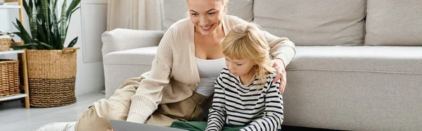 Счастливая блондинка смотрит фильм на ноутбуке рядом с дошкольником дочь в современной гостиной, баннер — стоковое фото