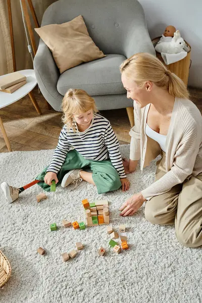 Маленька дівчинка з протезною ногою сидить на килимі і грає з дерев'яними іграшками біля щасливої матері — стокове фото