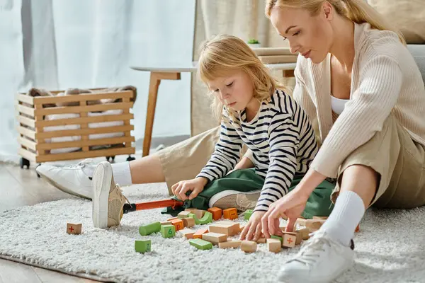 Blonde girl with prosthetic leg sitting on carpet and playing with eco wooden blocks near mother — Stock Photo