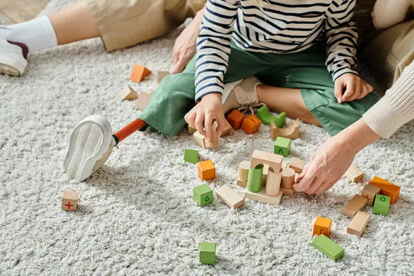 Colpo ritagliato, ragazza con gamba protesica seduta su tappeto e giocare con blocchi di legno vicino alla madre — Foto stock