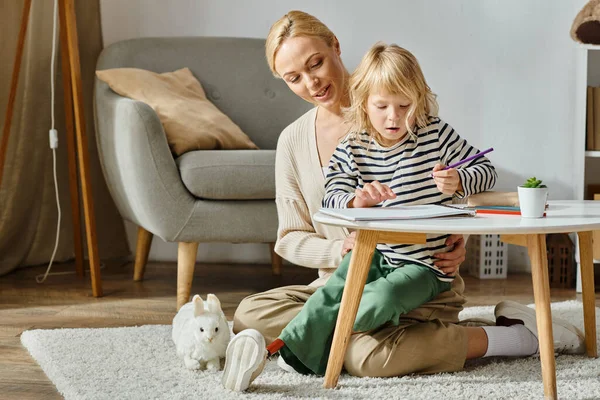Блондинка с протезной ногой рисует на бумаге с красочными карандашами рядом с поддерживающей матерью — стоковое фото